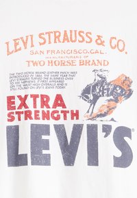 Balta medvilnė marškinėliai su retro stiliaus ekraniniu spausdinimu oranžine, raudona ir tamsiai mėlyna spalvomis, pabrėžiančius Levi Strauss & Co. prekės ženklą.