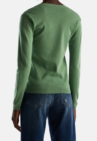 Grön, långärmad tröja med rund halsringning, gjord av ett mjukt, texturerat tyg. Matchas med blå, löst sittande jeans.