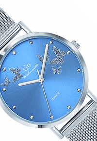 Montre en quartz bleue avec un bracelet en maille métallique argentée, accents en forme de papillon et marqueurs studieux sur un cadran texturé.