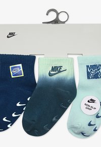 Tres pares de calcetines Nike: azul marino, azul teal degradado y verde menta. Cada uno presenta un diseño de colocación de logo y patrones distintos. Detalle de agarre antideslizante visible.