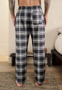 Sort-hvide ternede pyjamasbukser med elastisk talje, løs pasform og en baglomme, lavet af et blødt, åndbart stof.