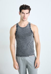 Grå tanktopp med en jevn tekstur, med rund hals og lett falmede kanter. Båret med grå joggebukser.