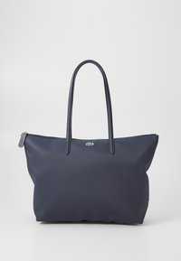 Sac fourre-tout bleu marine en matériau texturé avec deux poignées solides et une fermeture éclair. Présente un petit logo vert sur le devant.