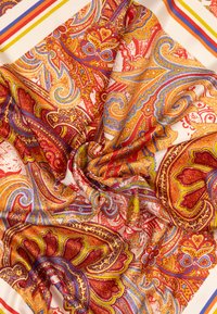 Écharpe en soie présentant des motifs cachemire vibrants en rouge, orange et bleu, avec une texture lisse et un tombé doux sur fond crème.