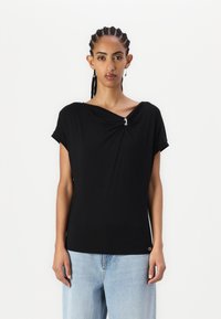 Top nero a maniche corte con scollatura a V, caratterizzato da un dettaglio annodato sul davanti e un accento decorativo in argento. Tessuto leggero e morbido.
