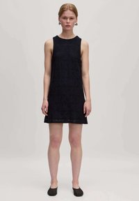Marineblaues ärmelloses Kleid mit einem strukturierten geometrischen Muster, knielang und mit geradem Saum. Kombiniert mit schwarzen flachen Schuhen.