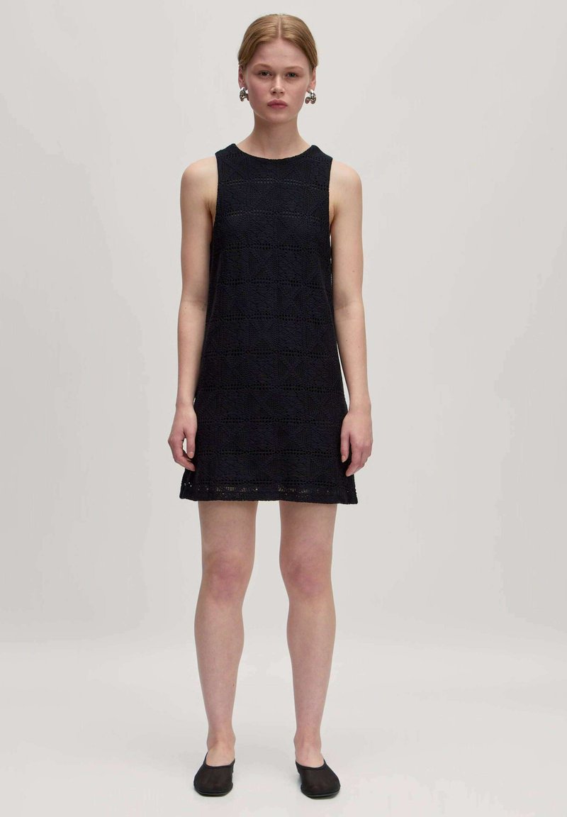 Marineblaues ärmelloses Kleid mit einem strukturierten geometrischen Muster, knielang und mit geradem Saum. Kombiniert mit schwarzen flachen Schuhen.