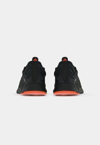 Chaussures de sport noires avec tige en maille texturée, accents réfléchissants et semelle en caoutchouc orange. La languette au talon présente un logo.