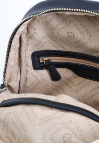 Černá kožená taška uvnitř s béžovou látkovou podšívkou. Disponuje zipovou kapsou a vzorem loga po celém povrchu. Zlacený zip.