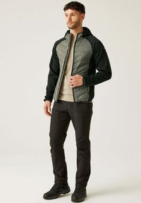Herren-Hybridjacke mit gepolstertem grauem Vorderteil und schwarzen Ärmeln, ausgestattet mit einem Reißverschluss vorne, Kapuze und dezentem Logo. Kombiniert mit dunklen Hosen und Stiefeln.
