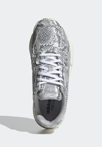 Grå och vit sneaker med en texturerad ormskinnsmönster, snörningsdesign, gummisula och en logotyp på tungan.