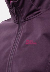 Veste softshell violette avec un col haut, fermeture éclaire à l'avant et logo rose. La texture du tissu semble lisse et légère.