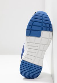 Suola di scarpa sportiva blu e bianca con gomma testurizzata, caratterizzata da tasselli rettangolari e un bordo liscio e arrotondato. Accenti neri sui lati.