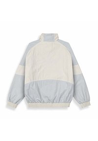 Chaqueta ligera de media cremallera en beige y gris claro. Presenta puños y dobladillo elásticos, con una textura suave y un diseño en bloques de color.