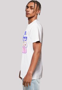 White cotton t-shirt featuring vibrant graphic print of fruits in pink and blue. Short sleeves and relaxed fit, with a crew neckline.