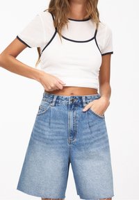 Biały top z krótkim rękawem z granatowym wykończeniem; luźne, jasnoniebieskie szorty dżinsowe z wysokim stanem, z surowym wykończeniem dołu i przednimi kieszeniami.