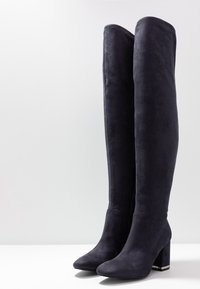 Mörk marina stövlar över knäet i mjuk mocka med en tjock klack, med en jämn textur och spetstopp. Enkel design utan utsmyckningar.