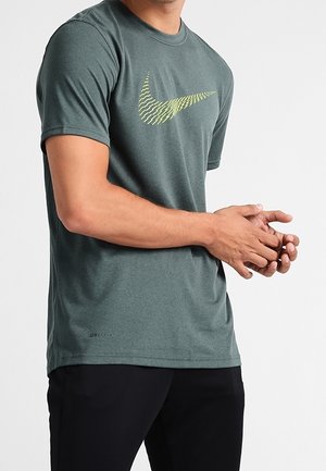Camiseta Nike verde de manga corta con un patrón de logotipos de swoosh amarillos. Fabricada con tejido transpirable, tiene un corte regular y una textura suave.