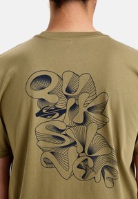 Camiseta de algodón verde oliva con un gran diseño gráfico abstracto azul en la parte posterior. Cuello redondo y mangas cortas. Textura suave.