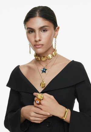 Guldtonet smykke har: chunky choker, lagdelte halskæder med en stjernet pendant og dristige ringe i forskellige former. Glatte, facetterede teksturer.