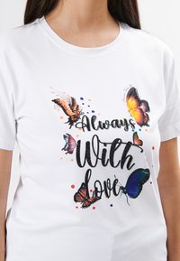 Hvid bomulds t-shirt med farverige sommerfugletryks og teksten "Alltid med kærlighed" i sort, pyntet med dekorative prikker.