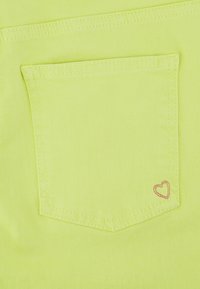 Neon gele denim stof met een opgestikte zak met een roze hartsteekdetail in de rechterbenedenhoek. Gladde textuur, stevige constructie.