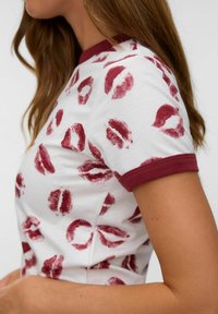 Hvid T-shirt med rødt læbeprint mønster, tætsiddende design og bordeaux ribbet krave og ærmekanter, der fremhæver en blød bomuldsstruktur.