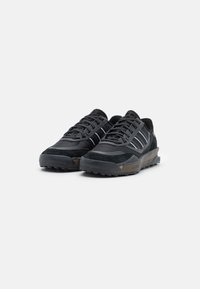 Zapatillas deportivas negras con un upper texturizado, que presentan tres rayas blancas, suelas gruesas y un patrón de dibujo resistente para tracción.