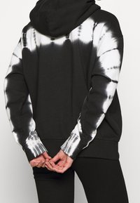 Sudadera negra con patrón de tie-dye blanco en las mangas, con capucha ajustable y puños acanalados. Fabricada con un tejido suave y texturizado.