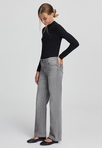 Jeans grigi ampi con vita alta e tasche classiche, indossati con una maglietta nera aderente a maniche lunghe e scarpe basse nere.