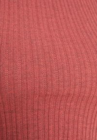 Gros plan sur un tissu côtelé tricoté rose rougeâtre avec des rayures verticales alternant entre des parties unies et en maille.