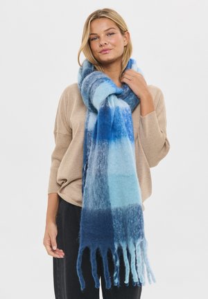 Lång, mjuk scarf i gradientnyanser av blått, med en texturerad yta och fransade kanter, bärs hängande runt halsen.