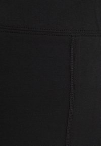 Svarta idrottstights i elastiskt tyg, med flatlocksömmar längs sömmarna för förstärkning och en mjuk yta.