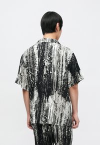 Majica s kratkimi rokavi z abstraktnim vzorcem v črno-beli barvi, s sproščenim krojem, odprtim ovratnikom in lahkotnim materialom.