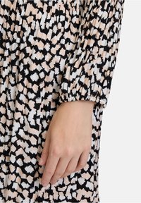 Langärmliges Kleid aus einem leichten Stoff, mit einem abstrakten Muster in Schwarz, Weiß und Pfirsich. Elastische Bündchen und geraffte Textur.