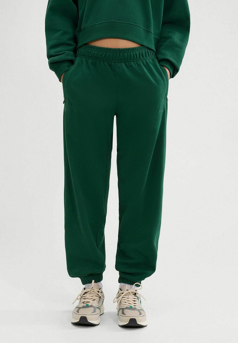 Pantalones de chándal verdes con cinturilla elástica y bolsillos laterales, hechos de material suave. Los puños ajustados en los tobillos completan el diseño.