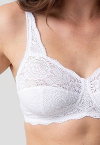 Witte kanten bralette met bloemenpatroon, golvende randen en verstelbare bandjes. Getextureerde stof met een semi-doorzichtige uitstraling.