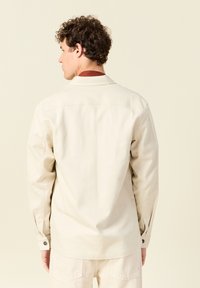 Beige katoenen overhemd met een rechte snit, lange mouwen, knoopmanchetten en een opgestikte kraag. Gladde textuur met minimale details.