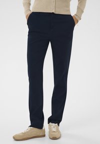 Tumed sinised püksid, mis on valmistatud siledast kangast, sirge lõikega. Omab küljetaskuid, vöörihmade silmuseid ja voldi esiosas.