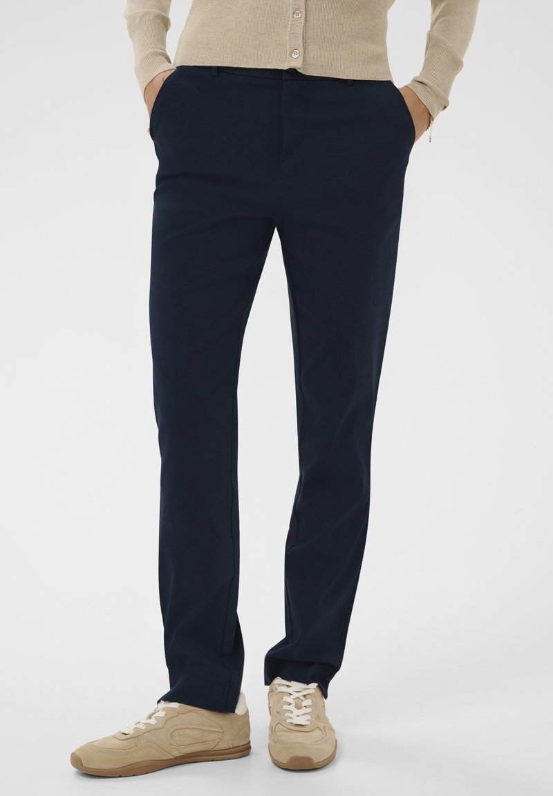 Tumed sinised püksid, mis on valmistatud siledast kangast, sirge lõikega. Omab küljetaskuid, vöörihmade silmuseid ja voldi esiosas.