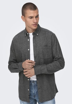 Dark gray button-up shirt made of textured fabric, featuring a chest pocket, white buttons, and cuffs, worn over a white t-shirt.