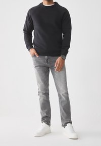 Sudadera negra con cuello redondo y mangas largas, combinada con jeans grises y zapatillas blancas. La tela parece suave con un acabado liso.