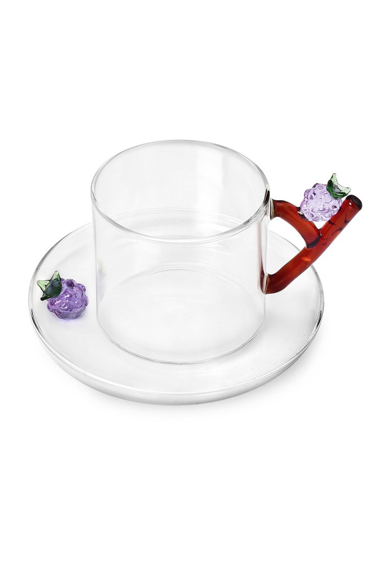 Przezroczysta szklanka z okrągłym dnem i uchwytem w kształcie gałązki, ozdobiona fioletowymi winogronami i zielonymi liśćmi, na dopasowanym spodeczku.