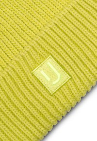 Gorro de punto en un amarillo brillante, con textura acanalada y una etiqueta cuadrada con un logotipo verde claro bordado en el lateral.