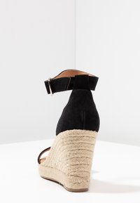 Sandalo con zeppa in suede nero, suola in corda di juta, cinturino alla caviglia con fibbia, superficie superiore liscia e design posteriore arrotondato.