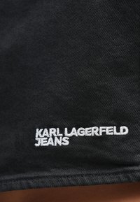 Čierna rifľová látka s bielym vyšívaným nápisom "KARL LAGERFELD JEANS" blízko dolného okraja.