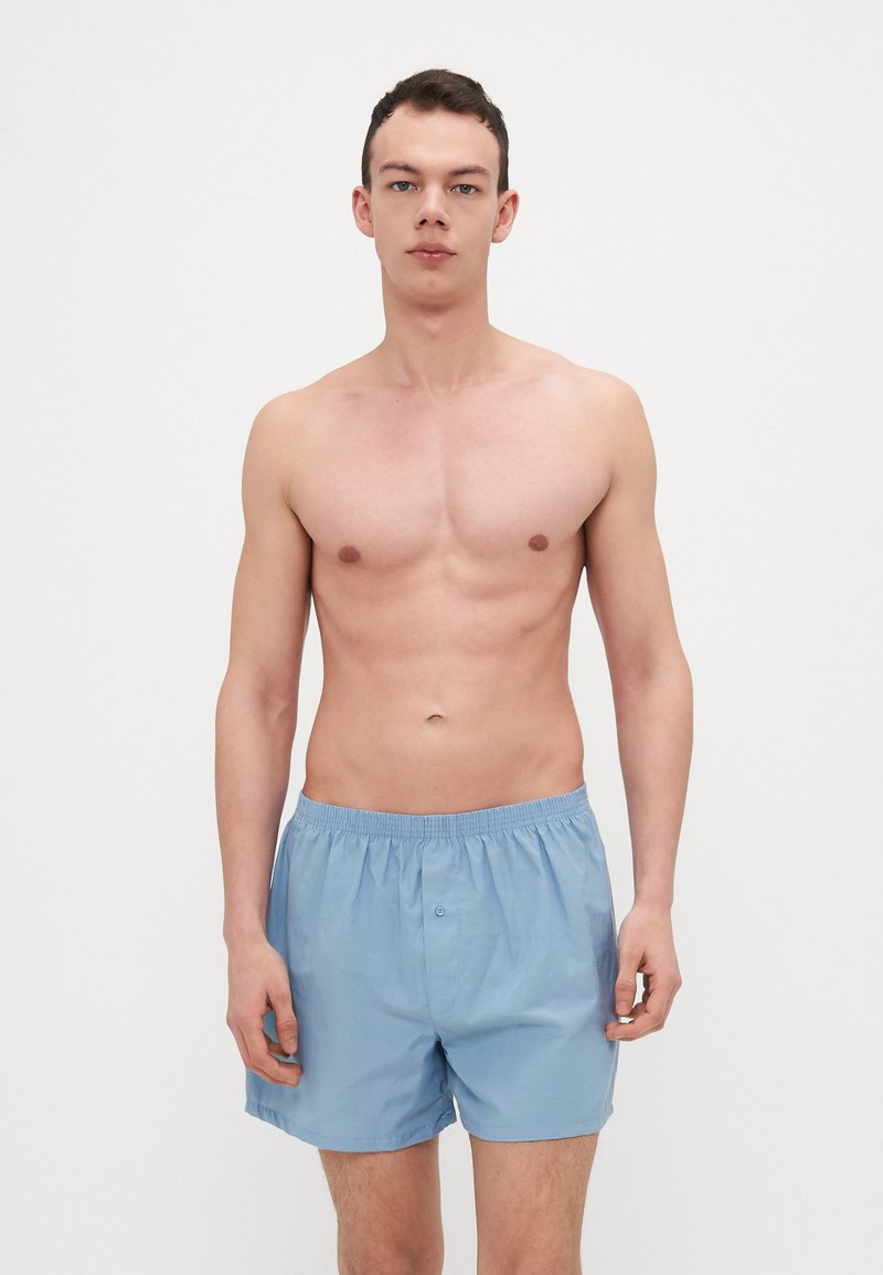 Shorts en coton bleu clair avec une taille élastique et une fermeture à bouton, présentant une coupe décontractée et un design minimaliste.