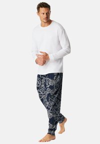 Camisa blanca de manga larga con cuello redondo, combinada con pantalones de pijama azul marino que presentan un patrón plateado de estrellas y formas abstractas.