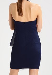 Marinblå axelbandslös klänning med en figurnära livstycke och en mjuk, svävande kjol. Har en diskret dragkedja bak och subtila veck.