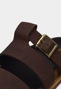 Sandale en cuir marron avec deux larges brides et une boucle en métal doré sur une bride pour un ajustement réglable.